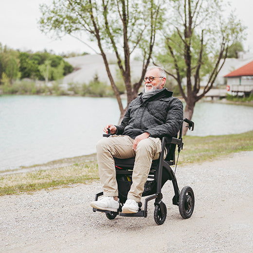 Man in a wheelchair by a lake with trees in the background