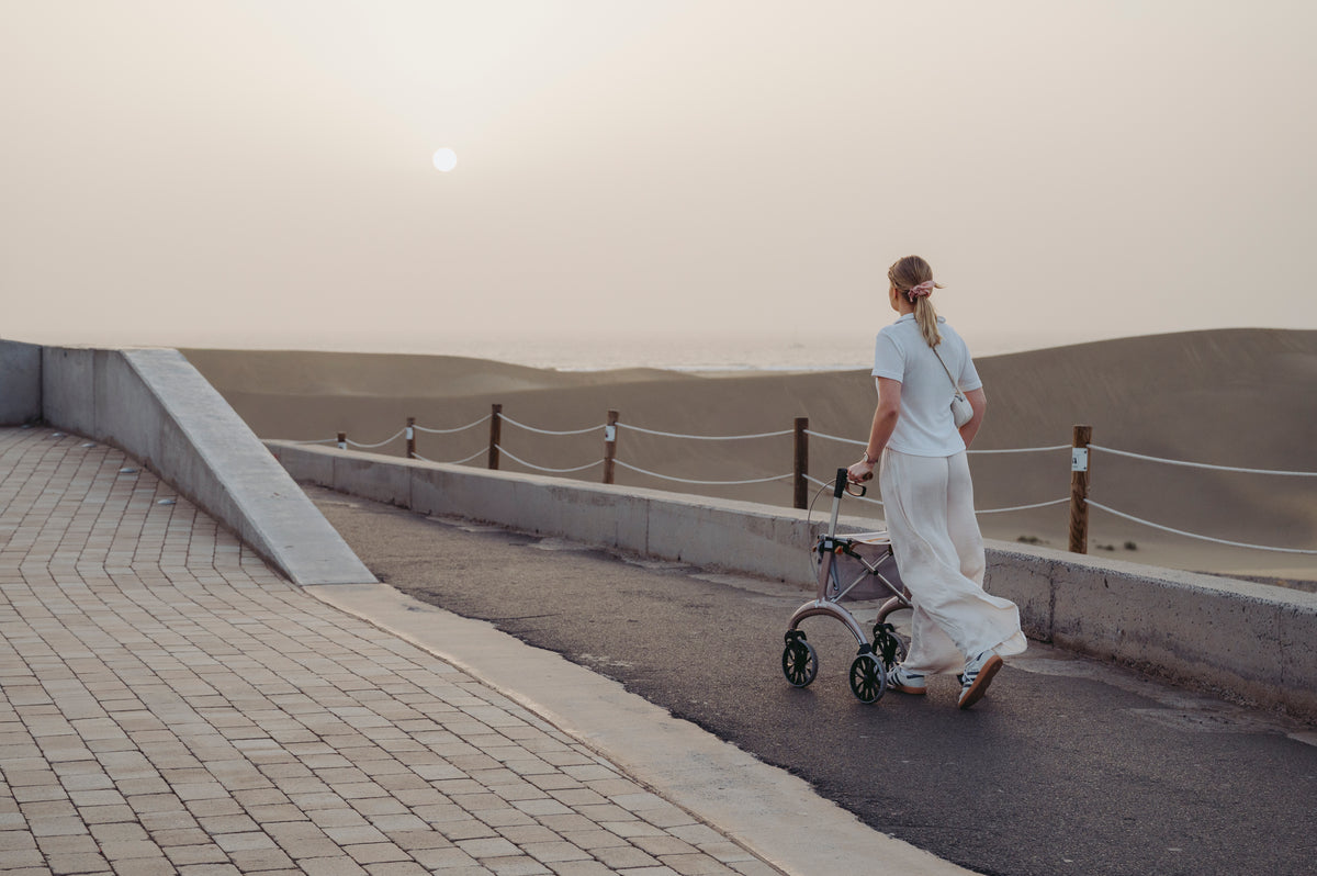 A woman walking with a Saljol Carbon Superlight rollator on a coastal path at dusk