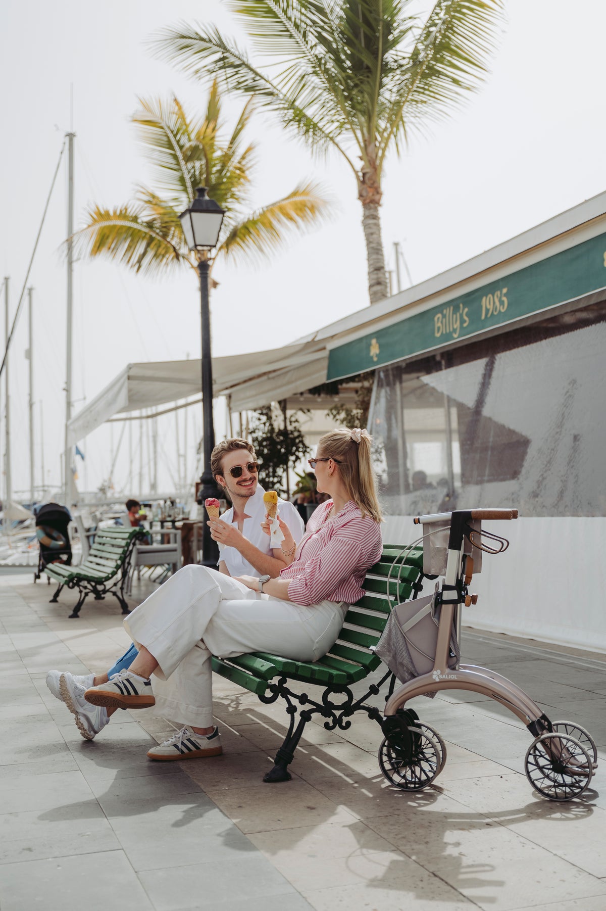 Two women sitting on a seafront promenade beside a Saljol Carbon Superlight rollator