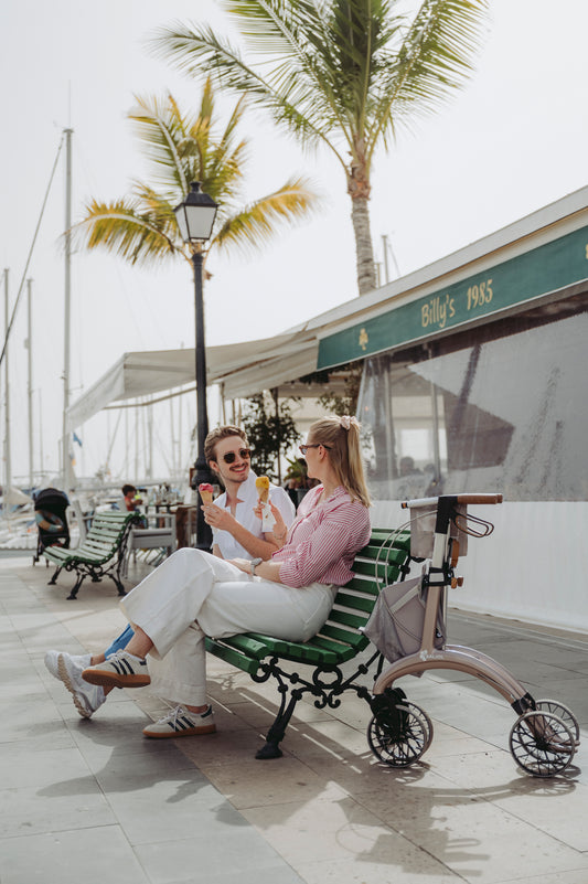 Two women sitting on a seafront promenade beside a Saljol Carbon Superlight rollator