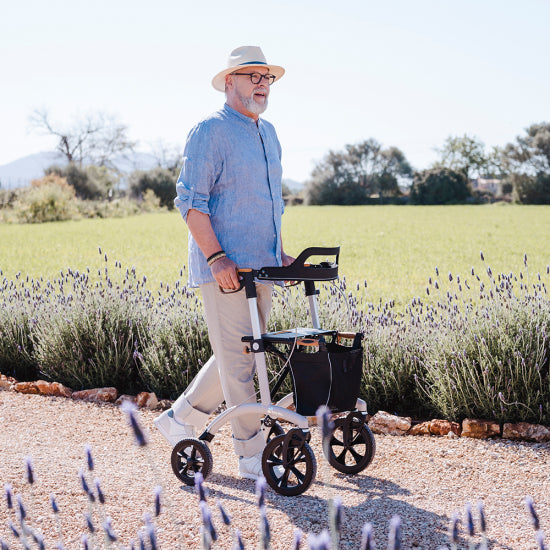 A man walking with a white Saljol rollator along a path beside a lavender field
